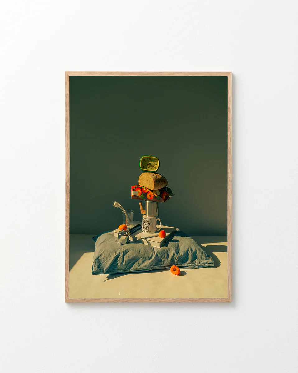 On a kitchen wall, the framed Its Time to Wake Up Poster displays a retro still life with canned fish, bread, and tomatoes artfully balanced on a mug atop a pillow. A small watering can and scattered tomatoes complete this breakfast scene against a minimal backdrop.