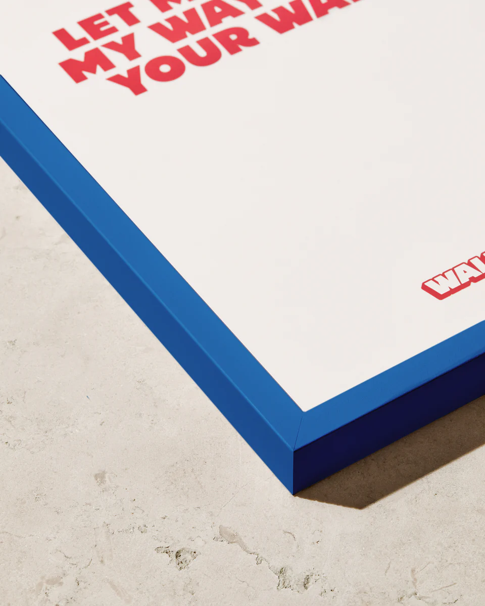 Close-up of the stylish Frame Blue poster in a blue wooden frame on a beige surface, featuring bold red text on a crisp white background.