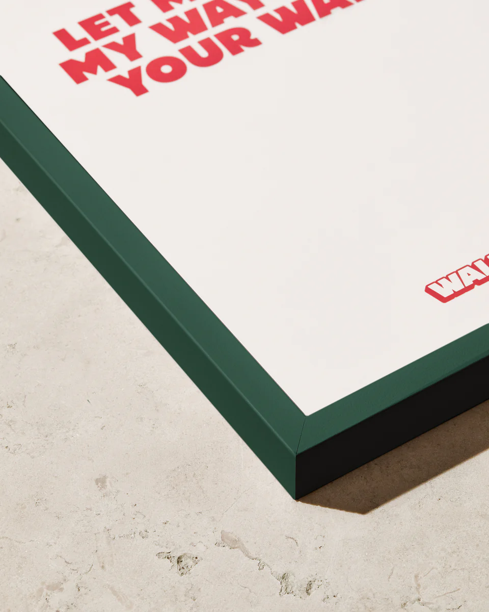 Close-up of a framed poster on a beige stone surface. The Frame Green adds a stylish pop with its dark green wooden frame, and the partially visible red text stands out against the white background.