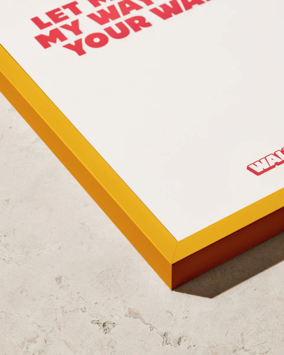 A close-up of the Frame Yellow poster showcases a stylish color pop with an orange frame on a textured light surface. Partial red text reads LET MY WAY BE YOUR WAY, though the rest is cropped out, making it a perfect complement for any space.