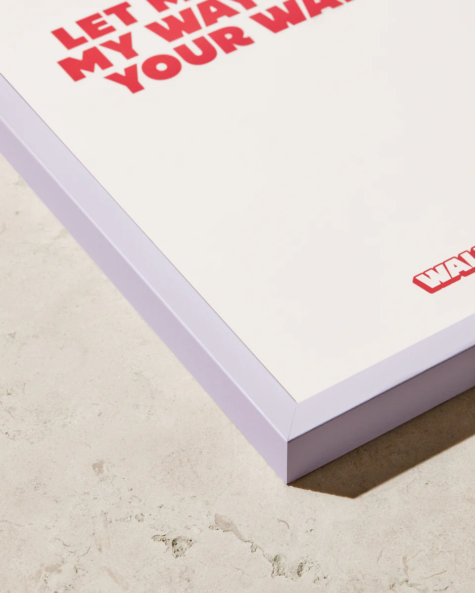 The artworks red letters on a white background are creatively enclosed within the Frame Pastel Purple, which adds a stylish pop against the light-colored, textured surface.