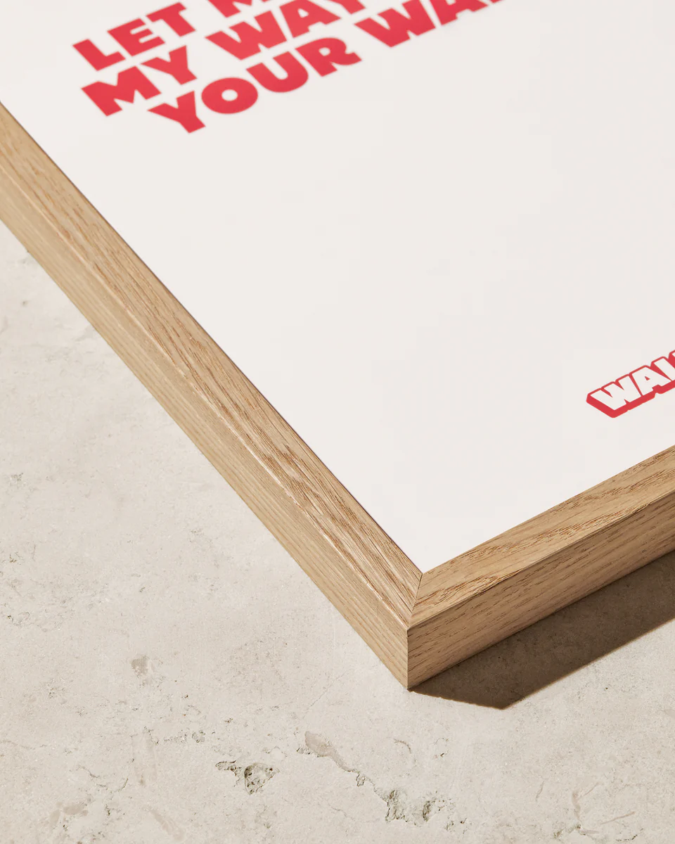 A close-up of a corner of the Frame Oak, elegantly resting on a light-textured surface. The wooden frame enhances its Scandinavian style, with red text partially visible on the white background.