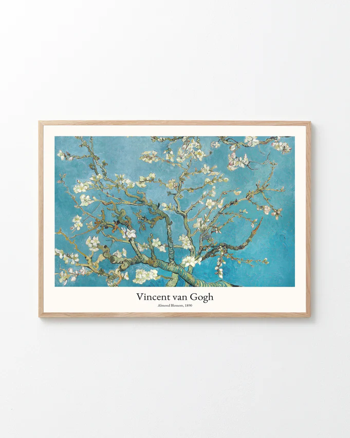 The Almond Blossom by Vincent van Gogh Poster hangs on a pristine white wall, featuring blooming almond branches against a vibrant blue sky, with the title and artists name elegantly displayed beneath the image.
