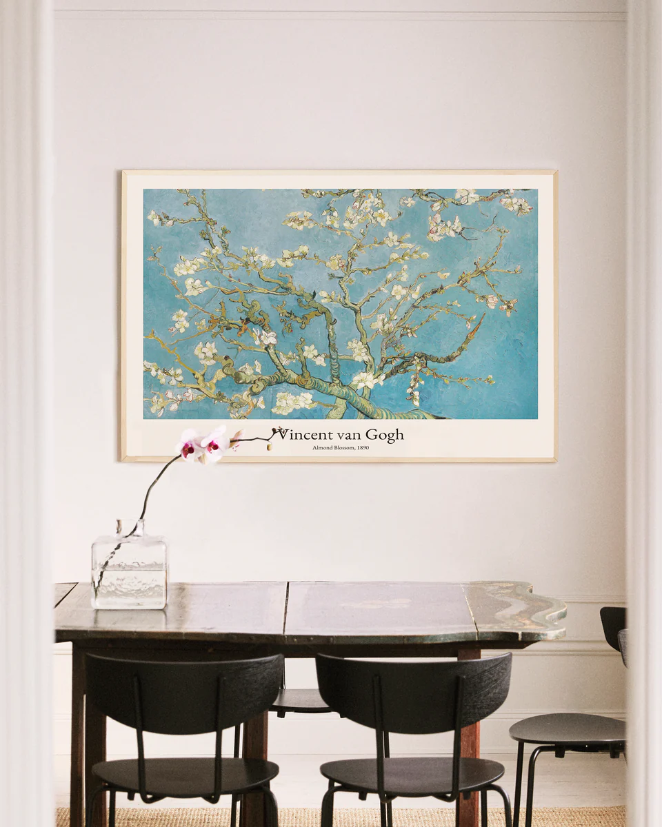 A dining area includes a wooden table and black chairs with a glass vase holding an orchid. An Almond Blossom by Vincent van Gogh poster is framed on a light wall, bringing elegance to the space.