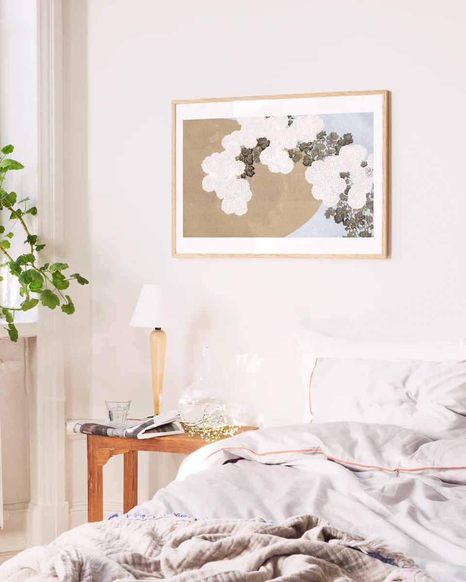 Neatly made bed with a side table and floral artwork on the wall in a bedroom setting.