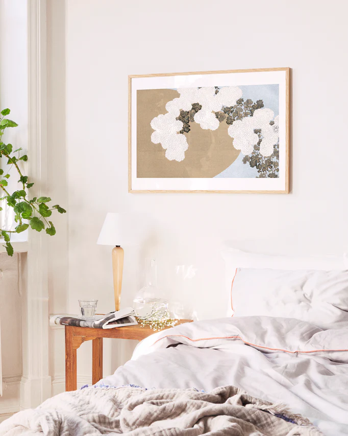 Neatly made bed with a side table and floral artwork on the wall in a bedroom setting.