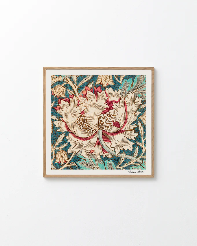The light wood-framed Honeysuckle by William Morris Poster displays a central cream and red flower with lush green leaves on a textured blue background, capturing the Arts and Crafts eras spirit against a plain white wall.
