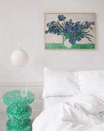 Framed artwork of Van Gogh's 'Irises' above a bed with a green side table.