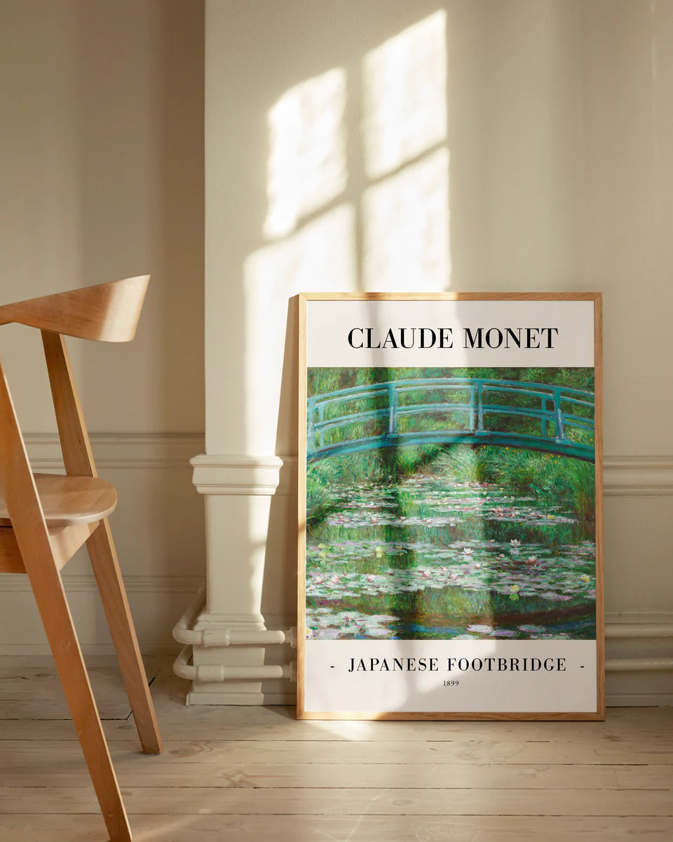 The Japanese Footbridge by Claude Monet 1899 Poster is a framed impressionist art print featuring a vibrant green arched bridge over water with lily pads, leaning against a sunlit wall next to a wooden chair.