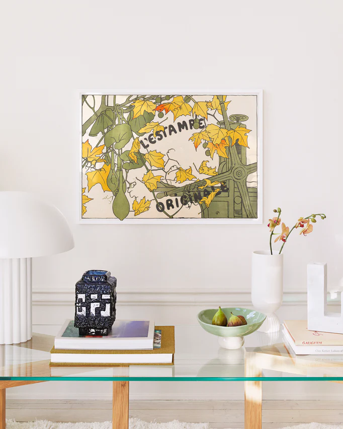 Decorative wall art with floral design and text above a glass table with books and a vase.