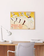 A minimalist office setup with a wooden desk, white lamp, and gray chair. On the wall hangs the poster La Troupe de Mademoiselle Eglantine by Henri de Toulouse-Lautrec, featuring dancers against a yellow background and capturing the charm of the Belle Époque era.