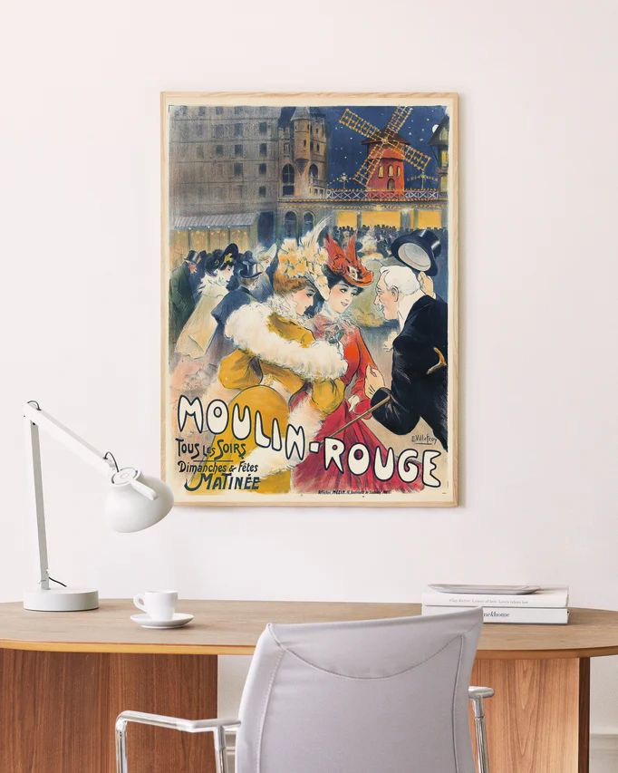 A stylish office features a wooden desk with a white task lamp, a gray chair, and an exquisite framed Moulin Rouge by E. Villefroy 1900 Poster, perfect for vintage art collectors who cherish colorful illustrations from that vibrant era.