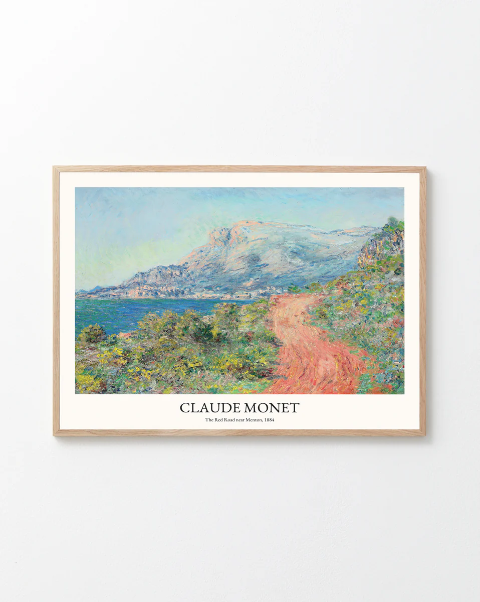 Framed print of Claude Monets The Corniche of Monaco showcasing Impressionist elegance, capturing a scenic landscape with a red dirt path, lush greenery, and coastal mountains against a white wall. This artwork beautifully reflects the charm of the French Riviera.