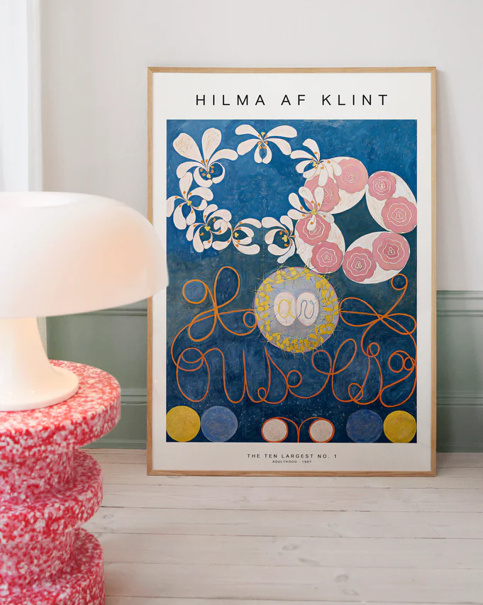 Framed Hilma af Klint artwork on a wall with a lamp and decorative table in the foreground.