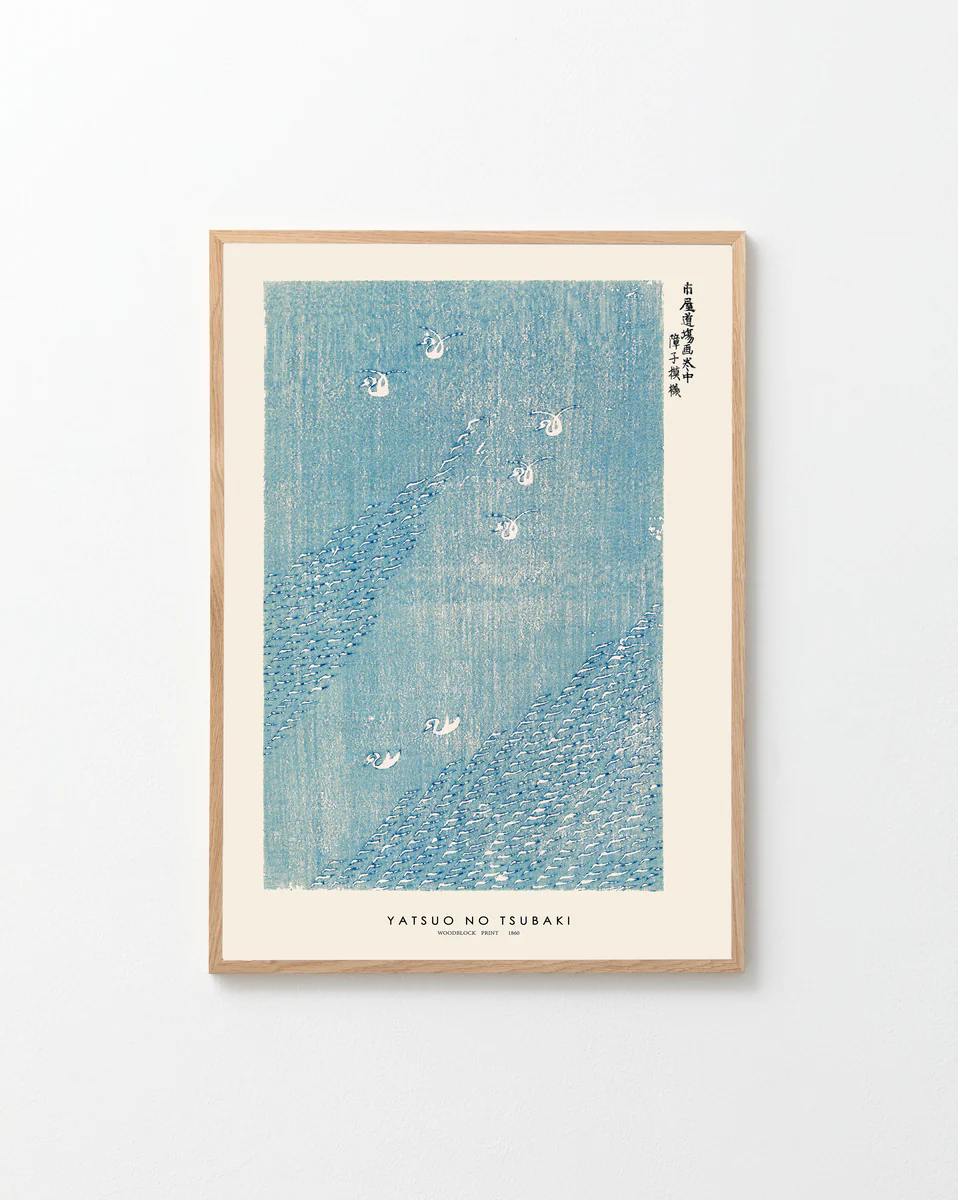The framed Woodblock Print Blue by Taguchi Tomoki Poster, a captivating Japanese artwork, graces a plain white wall. Its textured blue pattern with scattered white flowers evokes a classic woodblock print style. Elegant Asian characters embellish the top right.