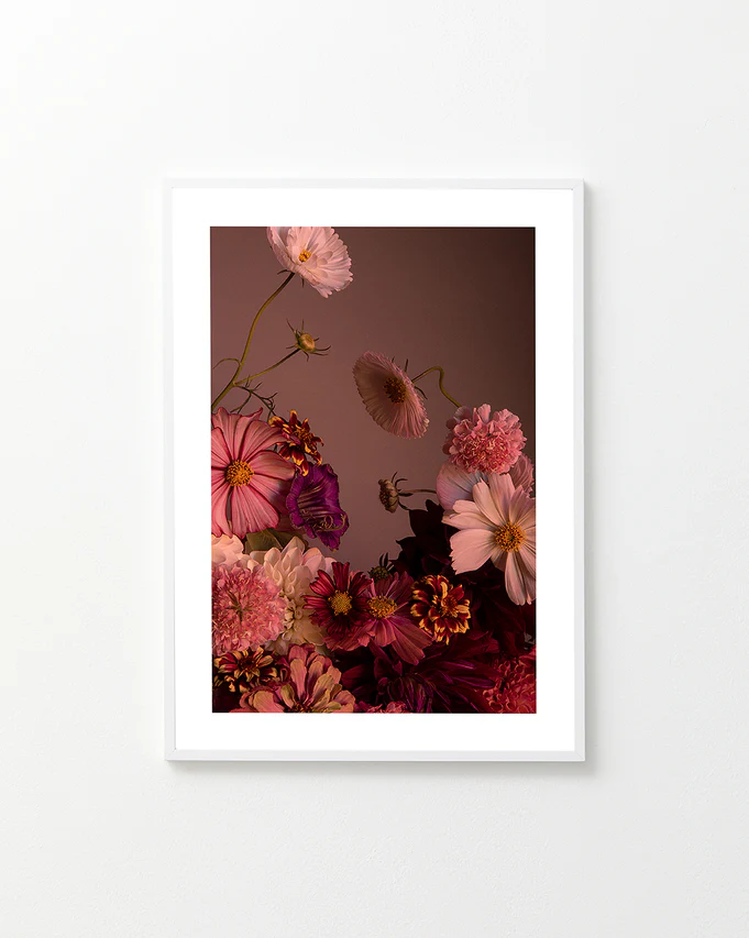 The Dreamscape Poster showcases a framed, vibrant floral arrangement of cosmos and zinnias in pink, red, and purple hues set against a muted brown background. Soft lighting highlights the elegantly arranged flowers and delicate petals.