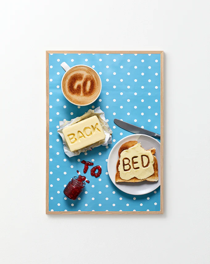 Poster "Go Back to Bed" in oak frame against a white background