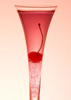 An eye-catching still life photograph showcasing a close-up of a drink adorned with a delectable cherry against a vibrant pink background.