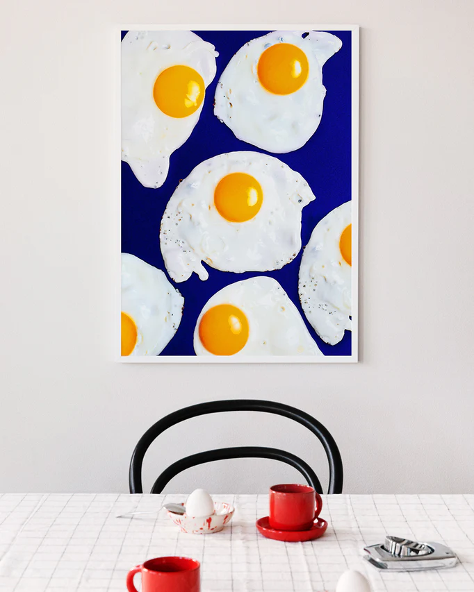 Poster "Eggs" in a white frame above a dining table