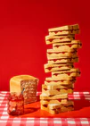 A tower of sandwiches and an empty jam jar on a red and white picnic cloth against a vibrant red backdrop