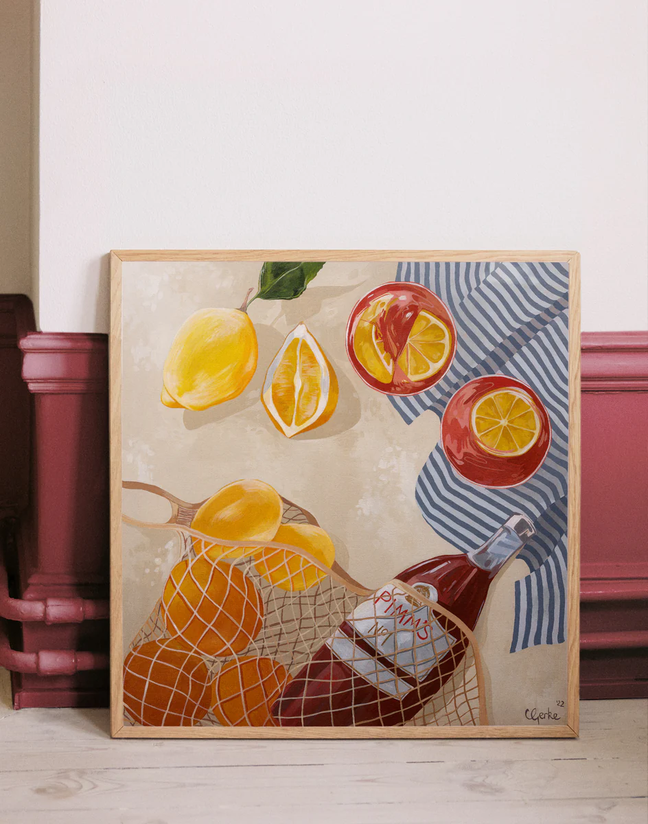 The Pimms Afternoon Poster, inspired by Cat Gerke, showcases a framed painting featuring sliced and whole lemons, a beverage bottle in a net bag, two glasses with red drinks on a blue and white striped cloth against a beige background with red wall accents.