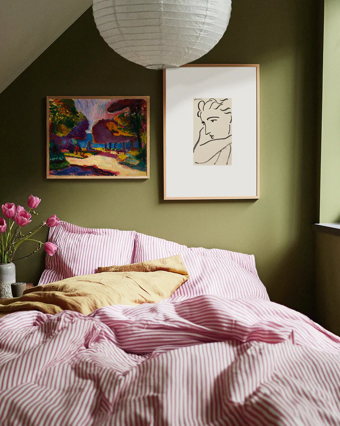 Bedroom with green walls, pink striped bedding, and framed artwork.