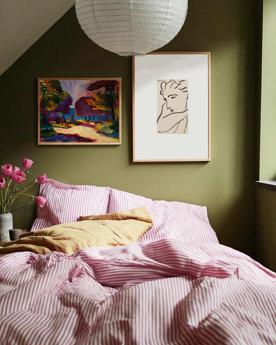 Bedroom with green walls, pink striped bedding, and framed artwork.