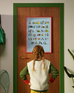 A child standing in front of a door looking at a Pippi Longstocking Swedish alphabet poster A–Ö.