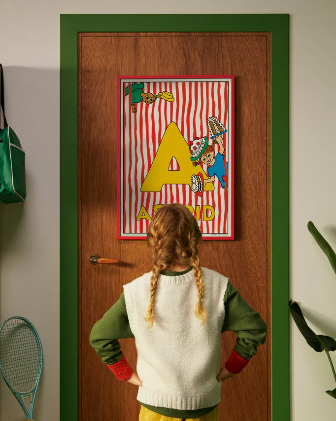 Pippi Longstocking poster featuring the letter A hanging on a door, with a child curiously looking at the artwork.