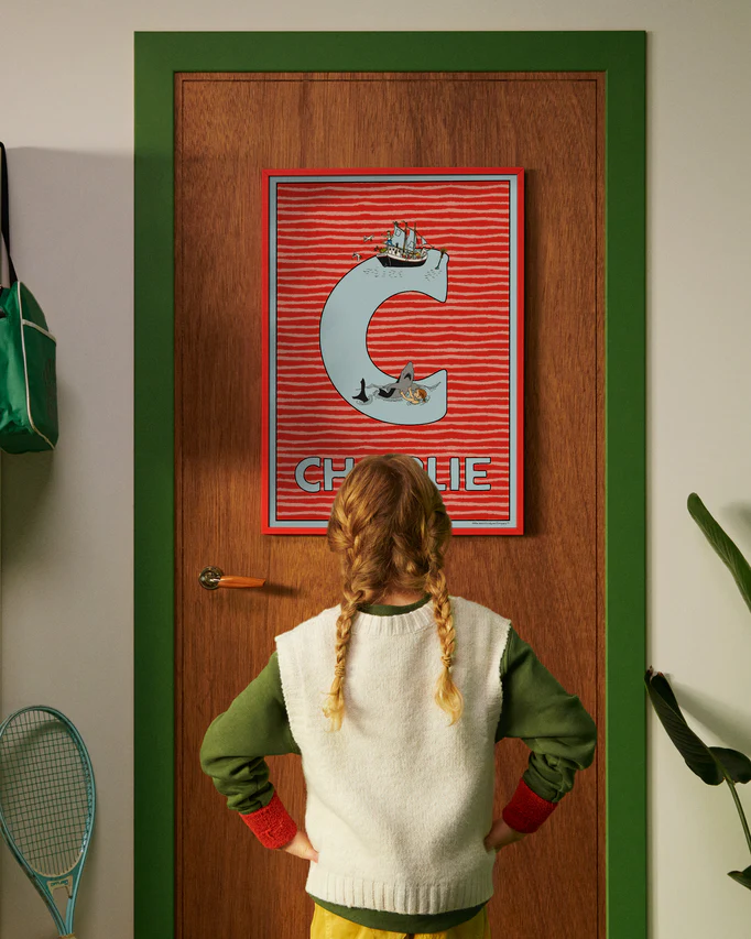 Pippi Longstocking personalised poster featuring the letter C hanging on a door, with a child curiously looking at the artwork.