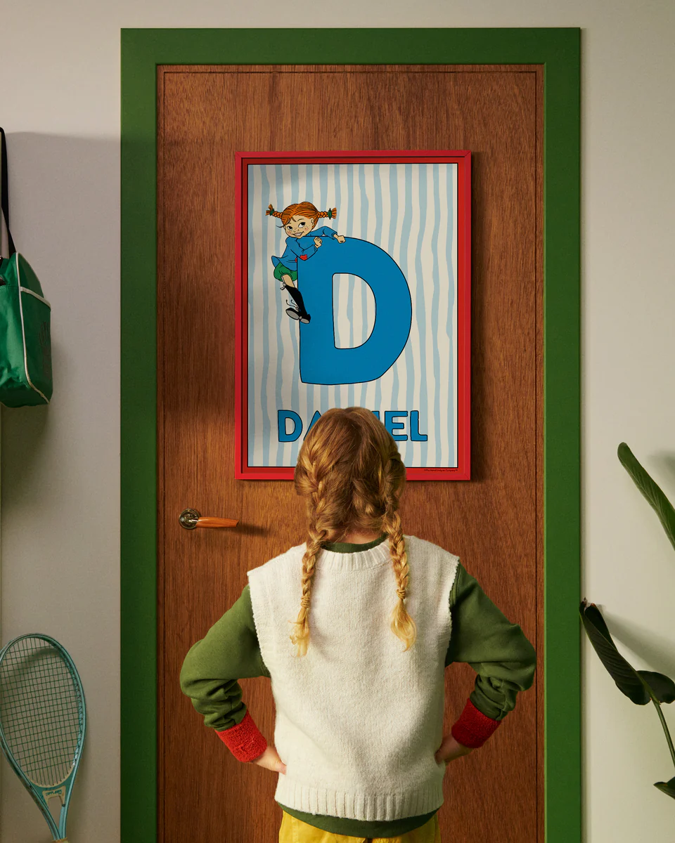 Pippi Longstocking personalised poster featuring the letter D hanging on a door, with a child curiously looking at the artwork.