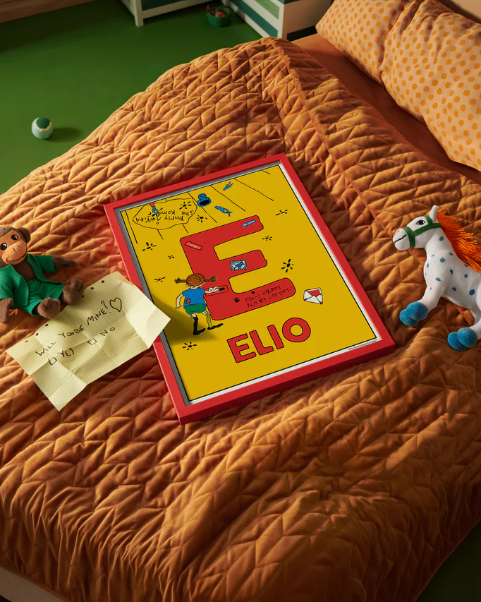 Pippi Longstocking name poster with the letter E and the name Elio, placed on a neatly made bed in a bright kids’ room.