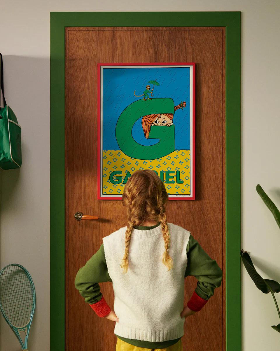 Pippi Longstocking personalised poster featuring the letter G hanging on a door, with a child curiously looking at the artwork.
