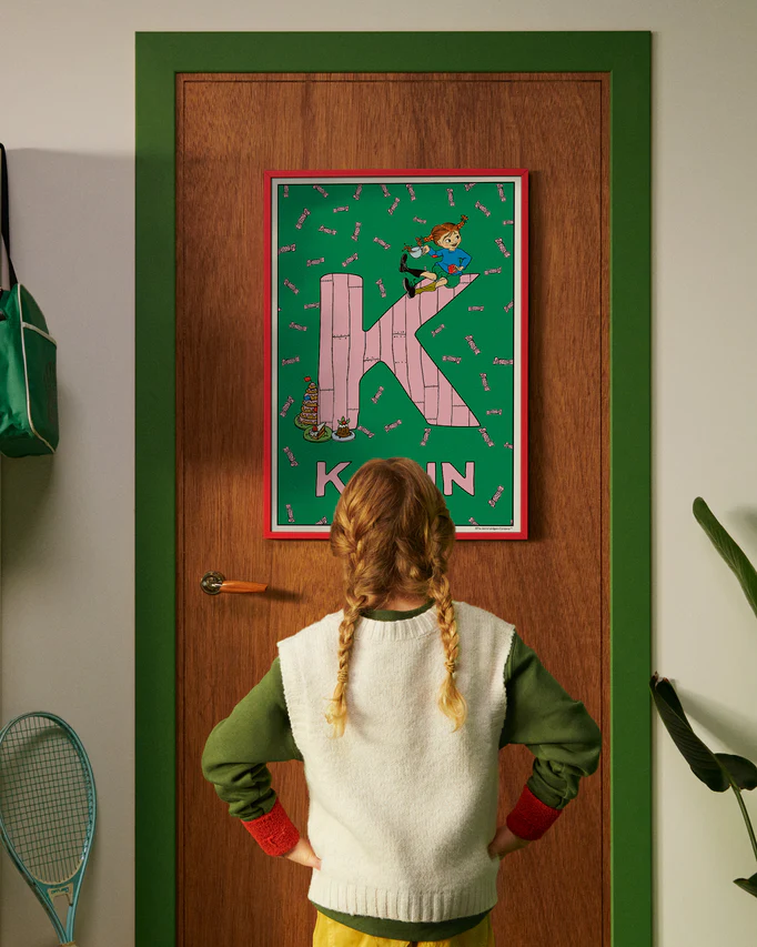 Pippi Longstocking personalised poster featuring the letter K hanging on a door, with a child curiously looking at the artwork.