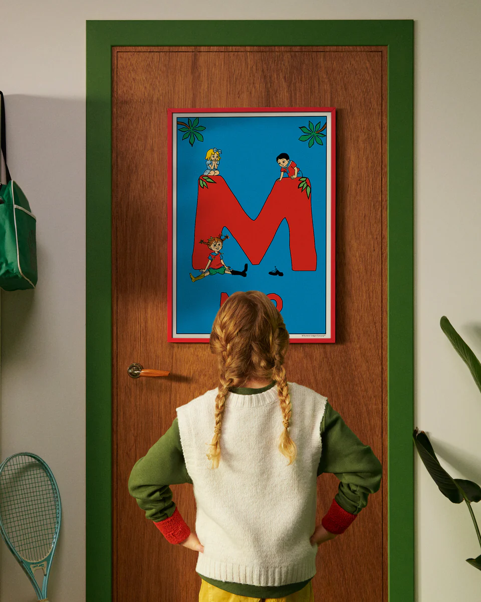 Pippi Longstocking personalised poster featuring the letter M hanging on a door, with a child curiously looking at the artwork.