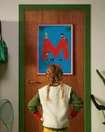 Pippi Longstocking personalised poster featuring the letter M hanging on a door, with a child curiously looking at the artwork.
