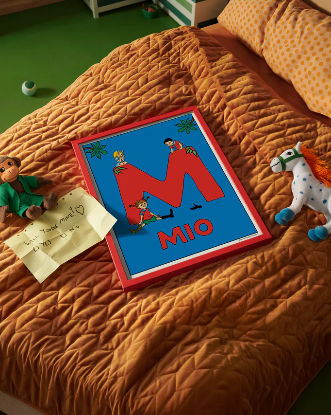 Pippi Longstocking name poster with the letter M and the name Mio, placed on a neatly made bed in a bright kids’ room.