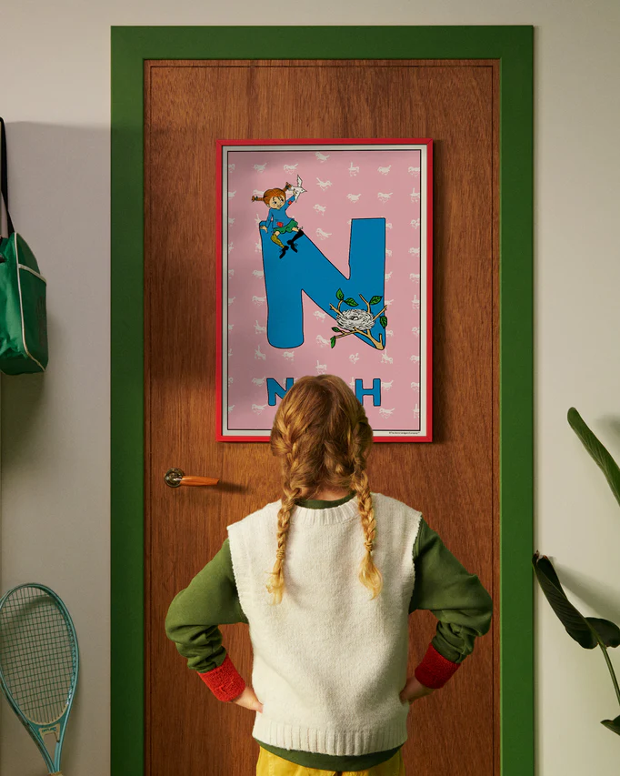 Pippi Longstocking personalised poster featuring the letter N hanging on a door, with a child curiously looking at the artwork.