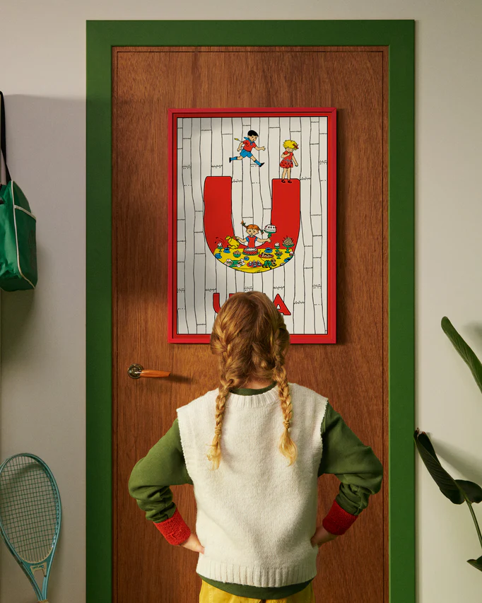 Pippi Longstocking personalised poster featuring the letter U hanging on a door, with a child curiously looking at the artwork.