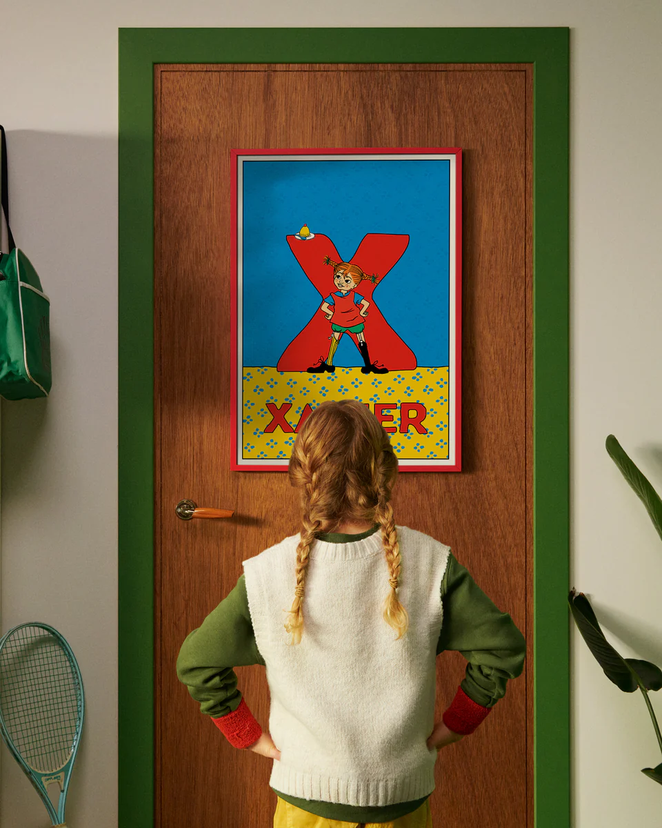 Pippi Longstocking personalised poster featuring the letter X hanging on a door, with a child curiously looking at the artwork.