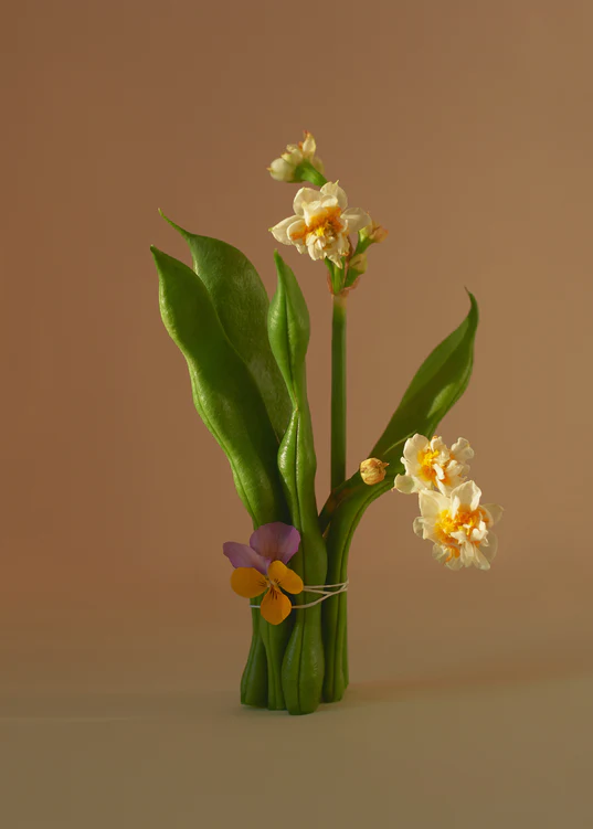 A still life against a light orange background featuring a bouquet made of sugar snap peas combined with flowers.