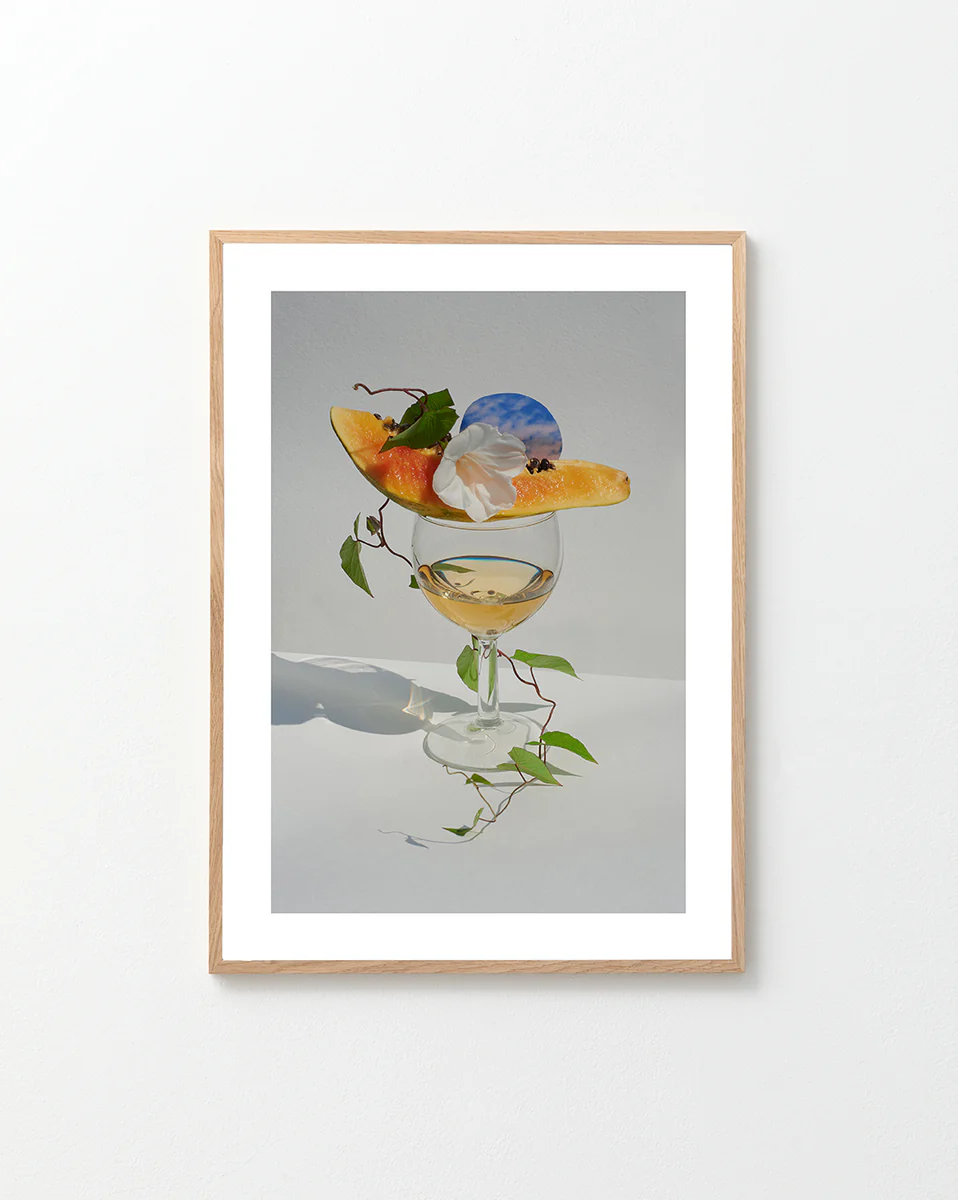 Poster featuring a stilllife photograph featuring a wine glas and on top a piece of papaya and a white flower in a oakframe