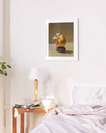 Poster featuring a stillife photography of a pear balancing on a plum in a white frame hanging above a bed