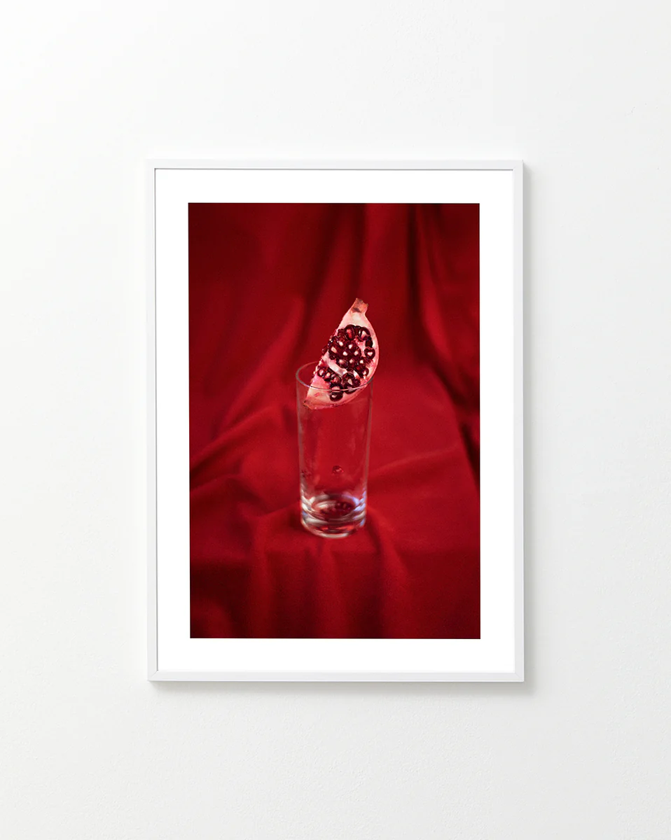 Slice of pomegranate in a glass standing on a blood red sheet.