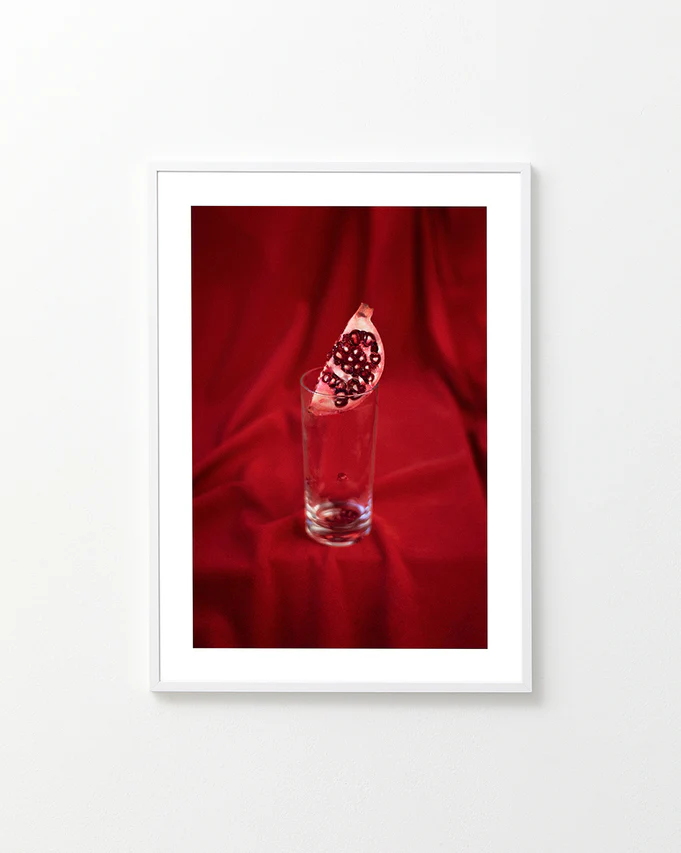 Slice of pomegranate in a glass standing on a blood red sheet.