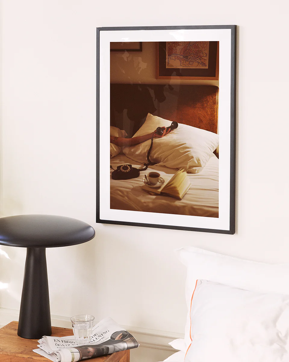 The Do Not Disturb Poster features a retro bedside scene with a coffee cup, glasses, open book, and vintage telephone above the bed. A nearby table with a water glass and magazine completes this nostalgic art piece.