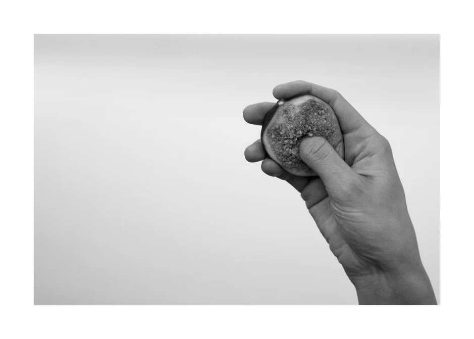 A hand holding half a fig and squeezing its flesh.