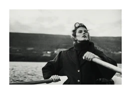 A woman in a thick coat rowing a boat on a black lake.