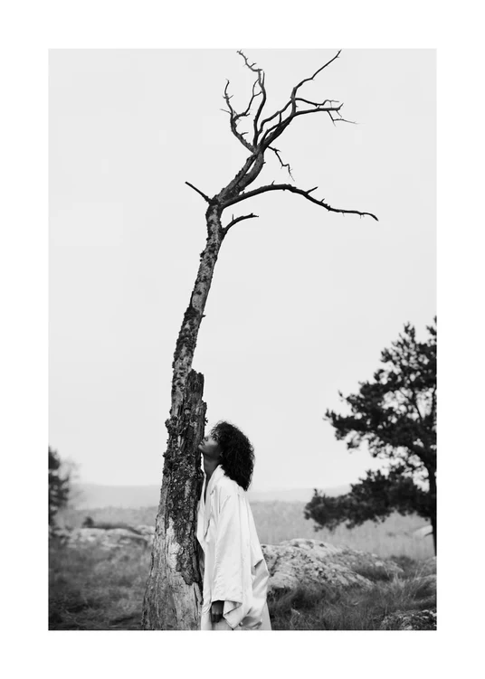 Black and white picture of a woman standing next to a dead tree.