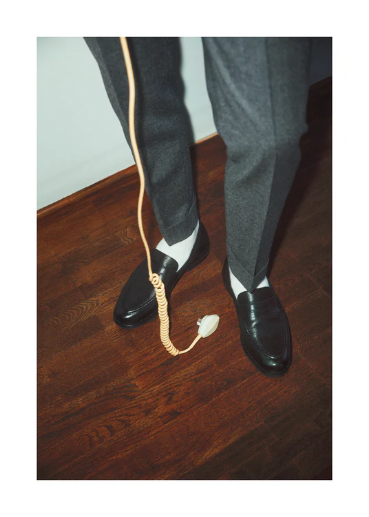 A man with dress shoes and slacks holding a yellow landline.